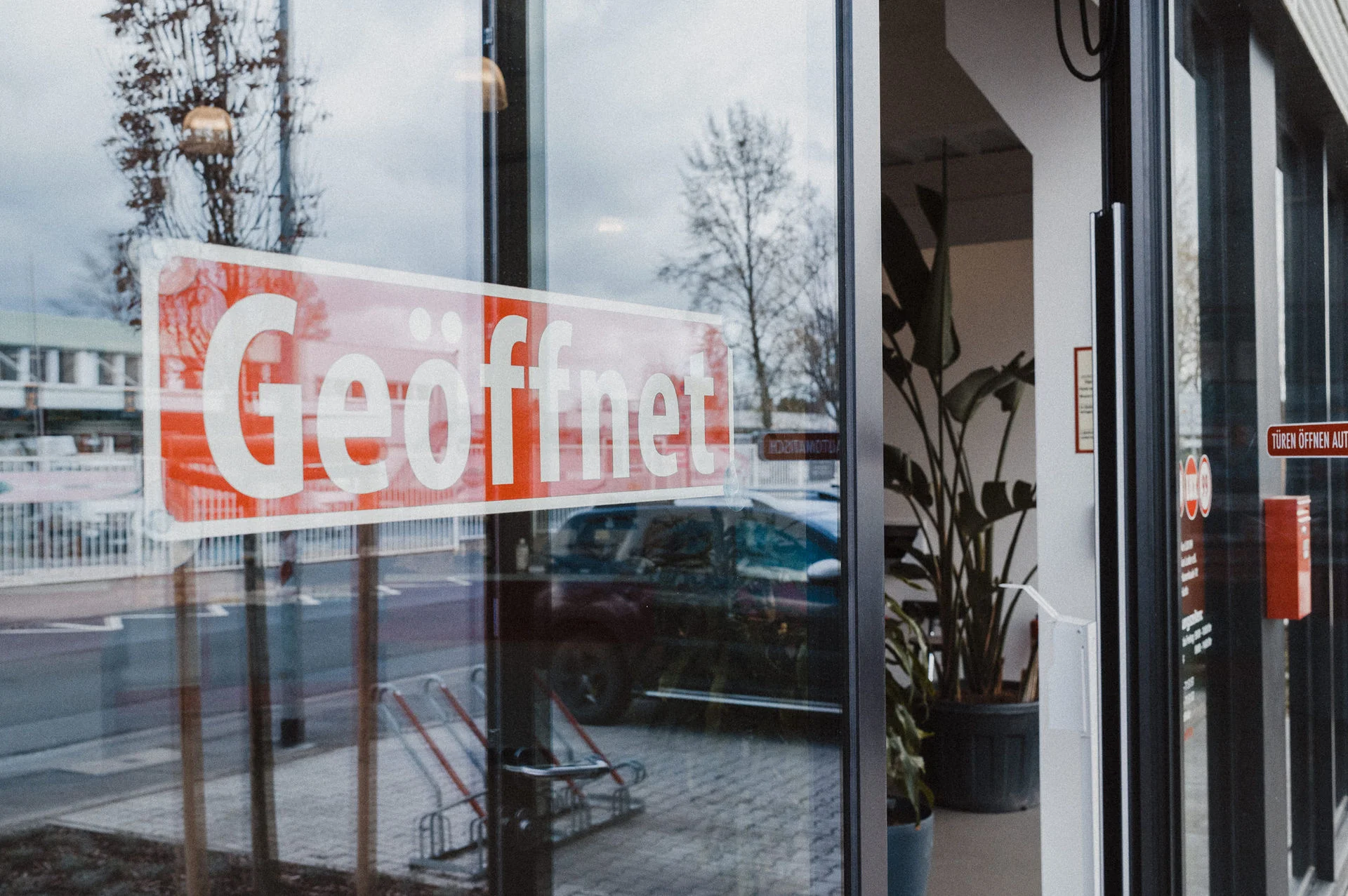 Ansicht des Apothekeneingangs mit großer Glasfront und Öffnungsschild. Der Eingangsbereich wirkt hell und einladend und bietet den Zugang zum Verkaufs- und Beratungsbereich der Apotheke.